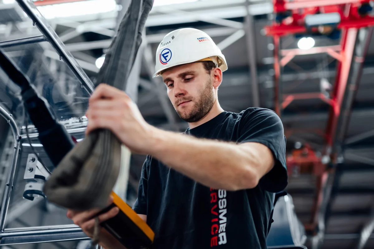 Fassmer Service employee at work in the shipyard: young man with safety helmet and Fassmer logo working focused on a component.